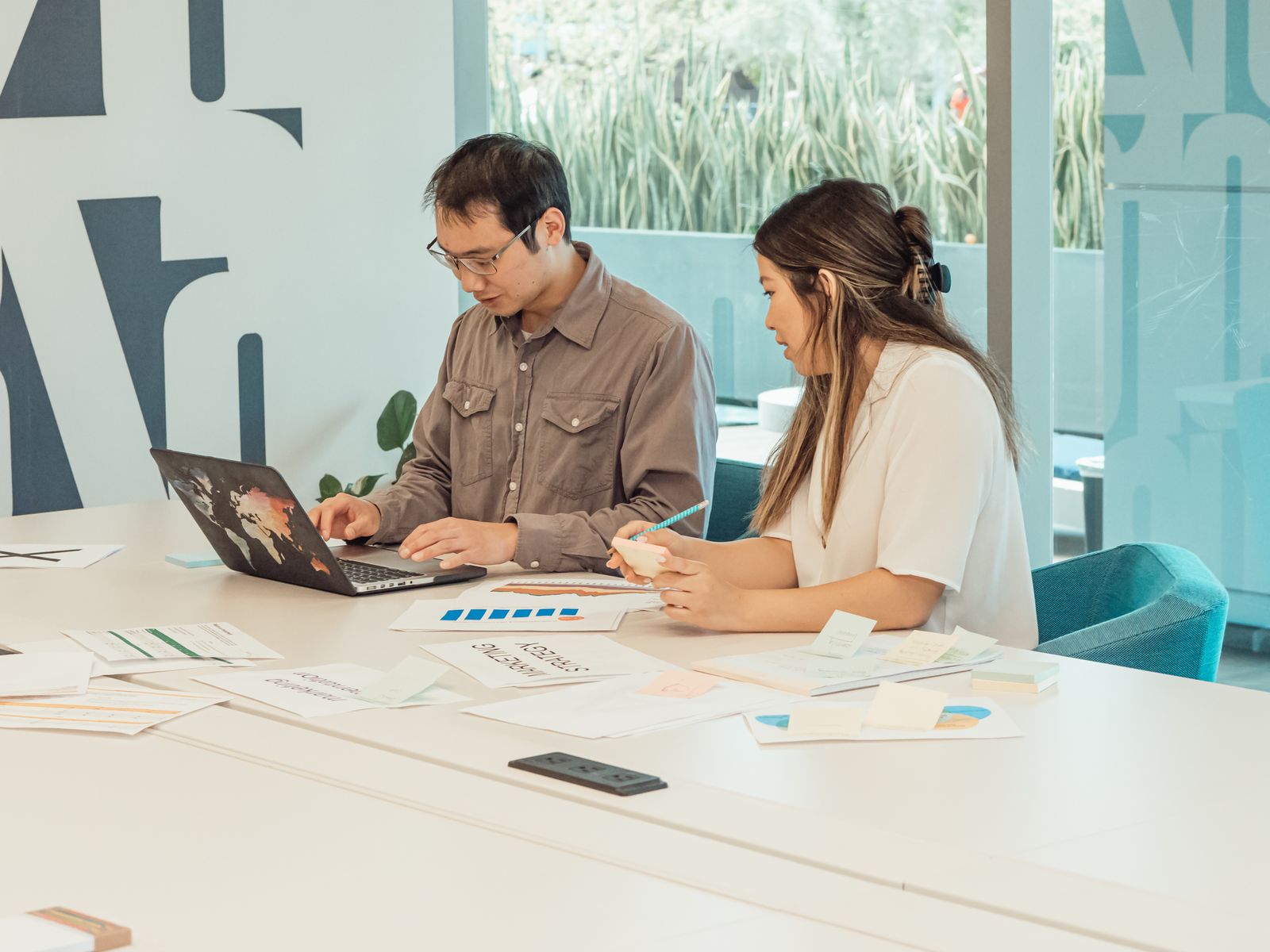 Two colleagues using a laptop and reviewing printed charts at an office desk